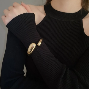 Close-up of a glossy gold teardrop open bangle showing its organic fluid metal design
