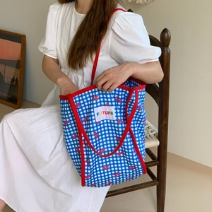 Blue plaid canvas tote bag with red bow print and FUTURE label shown on a wooden chair