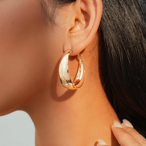Close-up of a chunky golden hoop earring with polished mirror finish on a model's ear