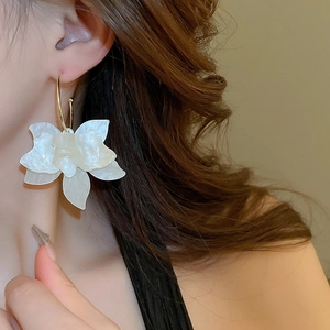 Detail of cream flower drop earring with pearl luster and gold hooks on a model