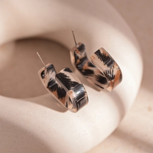 Macro shot of vintage leopard print resin hoop earrings displayed on a ceramic stand