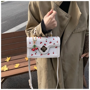 Détail du sac bandoulière blanc avec imprimé cerises et fermoir fleur doré élégant
