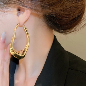 Close-up of golden irregular hollow earrings worn by model showing metallic luster