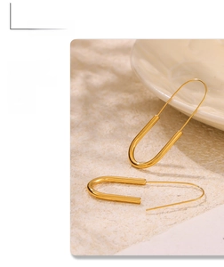 Detail of minimalist 18k gold plated stainless steel paperclip earrings on a beige background
