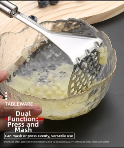 Macro shot of stainless steel potato masher mashing potatoes in a clear glass bowl