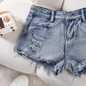 Detailed macro view of denim shorts featuring distressed rips and raw fringe hems on a sofa