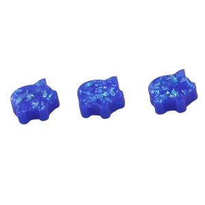 Three blue pig-shaped synthetic opal jewelry charms with glitter accents on white background