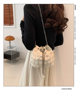Detail of white textured bucket bag with metal chain strap and pearl drawstring tassels