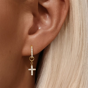 Macro shot of gold cross huggie earrings with sparkling crystals for women
