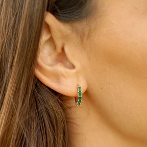 Elegant gold hoop earrings with rectangular green zircon stones worn by a model