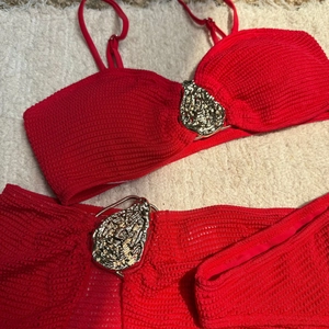 Detailed close-up of red ribbed knit bikini with artistic gold face-shaped metal buckles