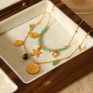 Detail of 18K gold stainless steel sea shell and starfish charms on a green beaded bracelet