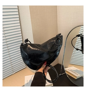 Close-up of black glossy half-moon saddle bag featuring pleated patent leather and knot detail