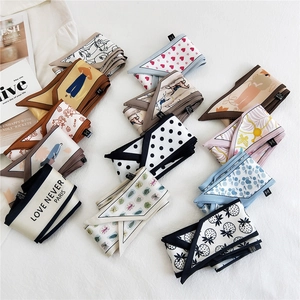 Various patterned silk-feel skinny scarves and ribbons arranged on a white surface