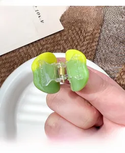 Close-up of a small gradient green and yellow resin hair claw clip with gold metal spring