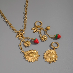 Detail of gold jewelry set featuring red enamel strawberry and sunflower charms