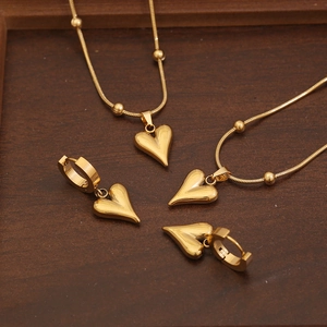 Golden heart pendant necklace set with matching earrings on a premium wood tray