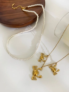 Detail of pearl necklace and gold crab pendant chain set on a dark wooden plate