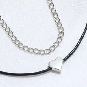 Macro detail of a double-layer heart pendant necklace with silver chain and black cord