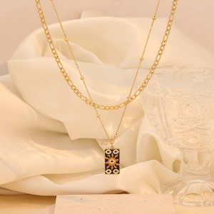 Close-up of double-layered gold necklace featuring a sun and evil eye rectangular pendant