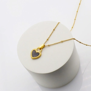 Close-up of heart-shaped black shell pendant with gold wave frame and bead chain necklace
