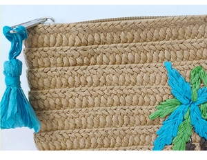 Close-up of khaki woven paper clutch featuring floral embroidery and blue tassel detail