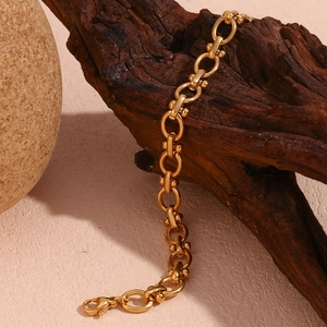 Détail du bracelet à maillons ovales plaqué or 18K sur fond de bois et pierre
