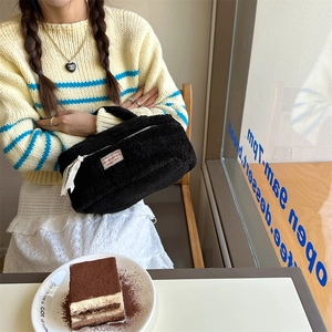 Close-up of a black fluffy plush makeup bag held by a person in a cozy cafe.