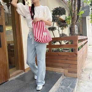 Close-up of red and white striped canvas tote bag with woven label in outdoor setting