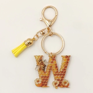 Detailed view of acrylic letter W keychain with bee hive pattern and yellow tassel charm