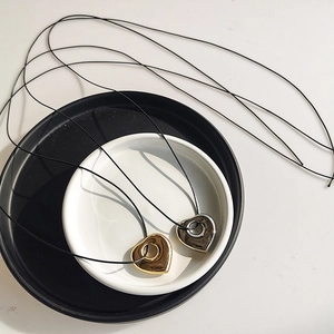 Detailed view of hollow heart pendants in gold and silver on minimalist black cords