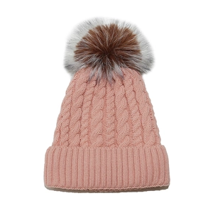 Detail of pink cable knit beanie with fluffy two-tone faux fur pompom and ribbed cuff