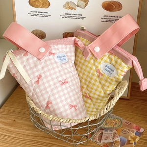 Close-up of quilted checkered pen bags with red bows and brand label in a basket