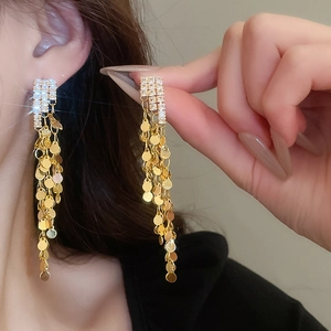 Close-up of golden long tassel earrings featuring sparkling crystals and metallic sequins