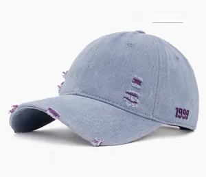 Detail of distressed light blue denim baseball cap with 1999 embroidery and torn edges