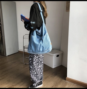 Detail of light blue denim tote bag featuring oversized front pocket and orange side tag