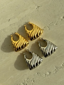 Macro detail of trapezoid hoop earrings featuring wavy textures in gold and silver finishes