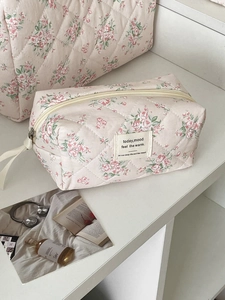 Beauty case trapuntati a fiori rosa con etichette in tessuto su espositore bianco a gradini