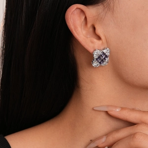 Detail of elegant silver stud earring with purple square zircon worn by model