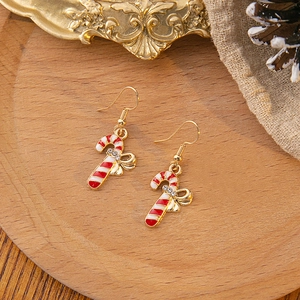 Christmas candy cane earrings with red white enamel and gold bow on wooden plate