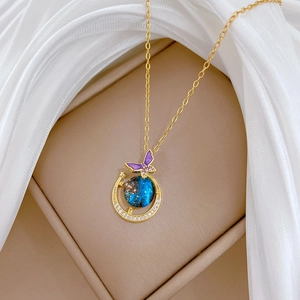 Detail of gold necklace with star-filled blue gem, crescent moon and purple butterfly