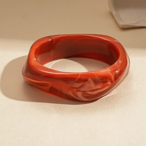 Détail d'un large bracelet en résine rouge foncé avec motif marbré et design torsadé