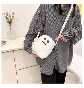 Détail d'un sac bandoulière en toile blanche avec broderie d'un visage de fantôme noir
