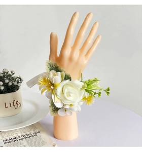 Detail of white artificial rose wrist corsage with green leaves for wedding accessories