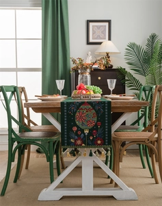 Detailed embroidery on green Christmas table runner with tassels on a wooden dining table