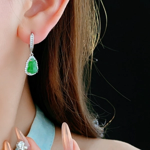 Close-up of elegant green zircon gourd earrings worn by a model on a dark background