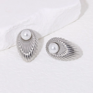 Detailed close-up of shell-shaped silver earrings with white pearls on a textured background