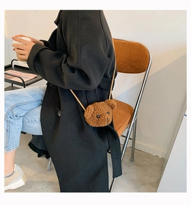 Detail of a brown plush teddy bear crossbody bag worn with a stylish black coat