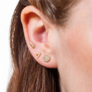 Close-up of gold geometric earring set including bar, triangle, and crystal studs