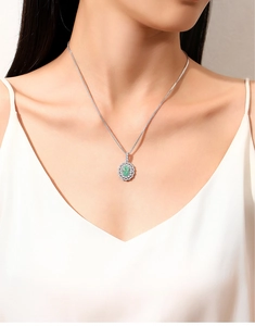 Detailed close-up of a halo-set green emerald pendant necklace worn by a model